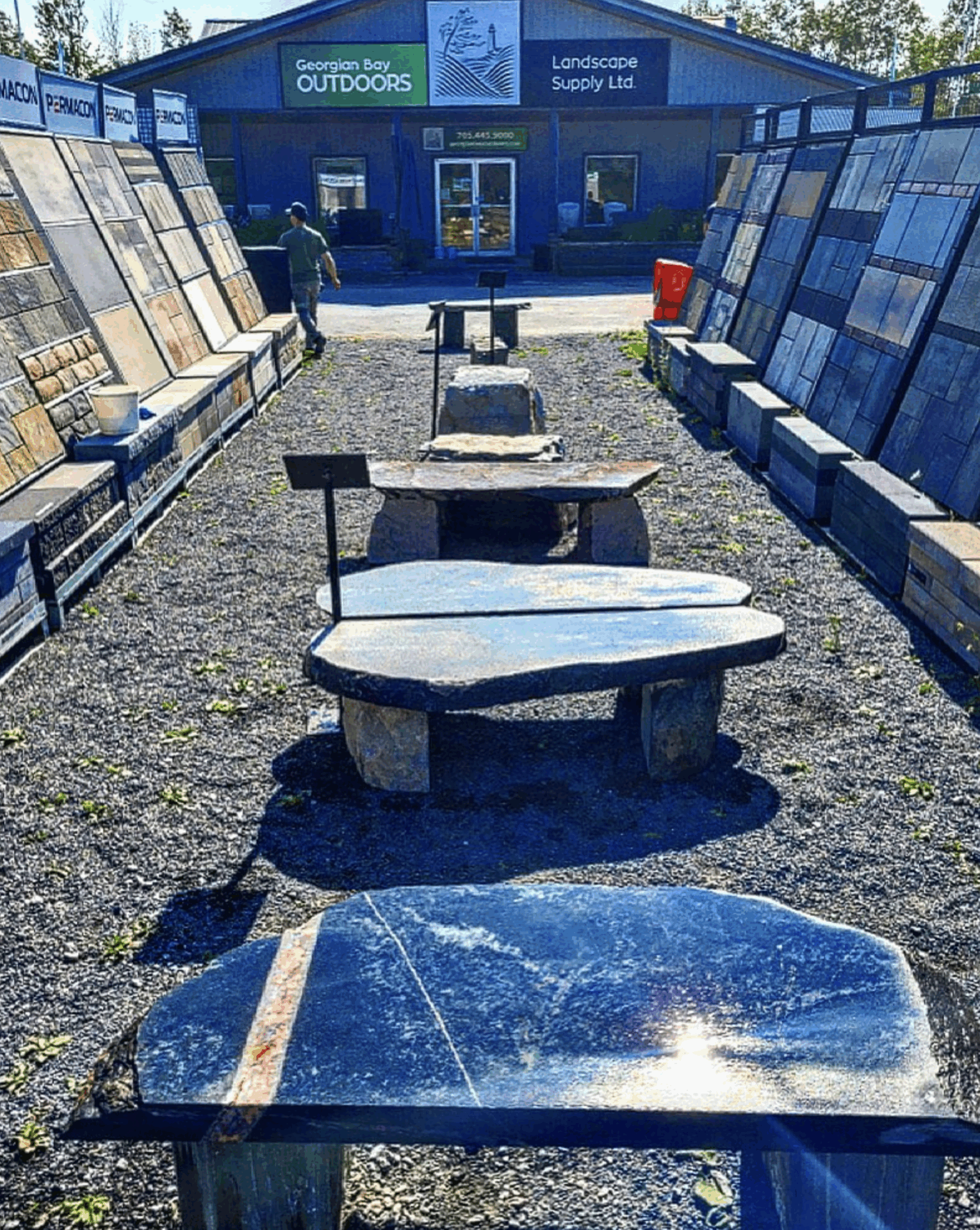 Outdoor display of stone slabs and tables at Georgian Bay Outdoors, Landscape Supply Ltd, with a person walking in the background.